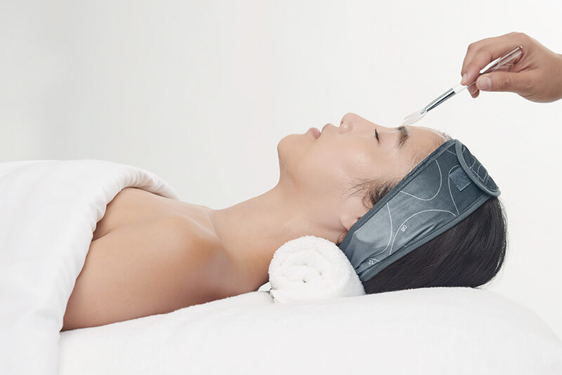Frau liegt mit weißem Handtuch im Nacken auf Behandlungsliege des Hautpflegestudios Harborg.