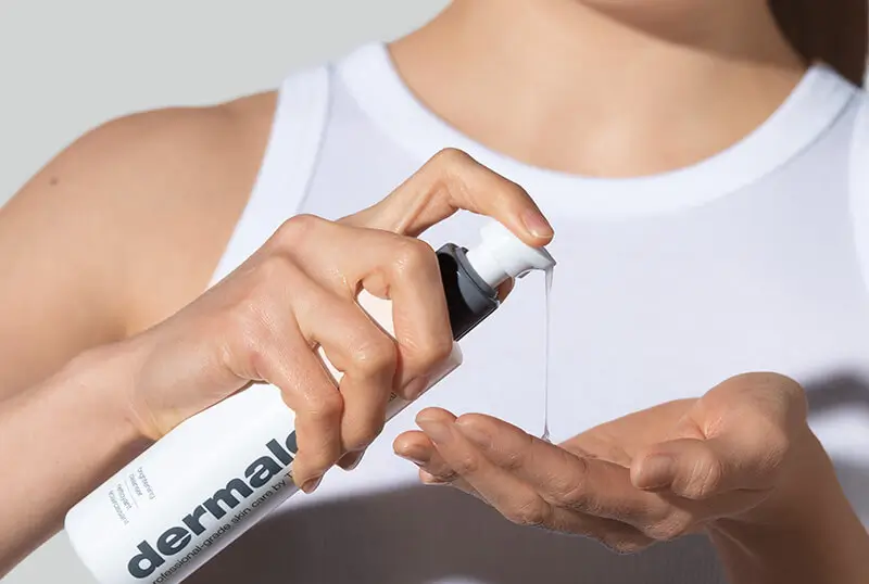 Eine Frau im weißen Top sprüht ein Hautpflegeprodukt von dermalogica in ihre linke Hand.